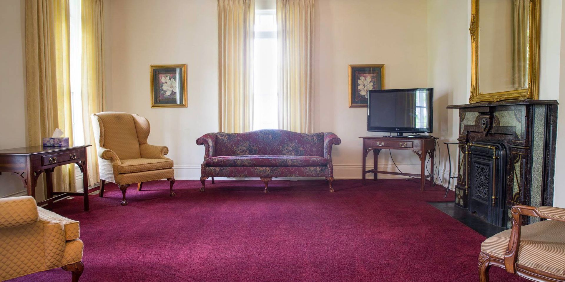 Elegant living room with burgundy carpet, cream walls, sofa, chairs, fireplace, and TV