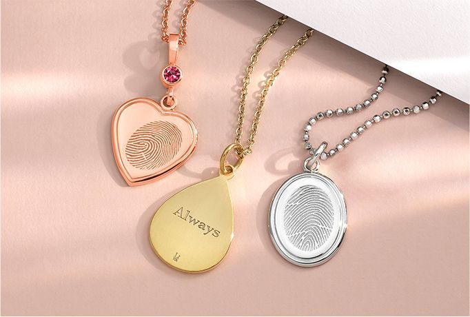 Three engraved heart and teardrop pendant necklaces in rose gold, gold, and silver on a soft pink background