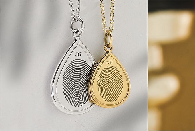 Silver and gold fingerprint teardrop necklaces with initials on a soft neutral background
