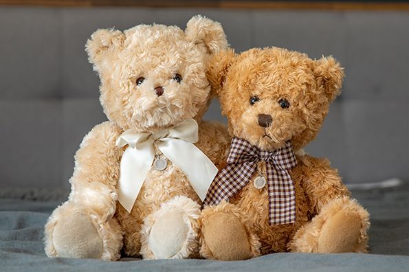 Two teddy bears sitting on a gray surface, one cream and one brown, each with a ribbon bow.