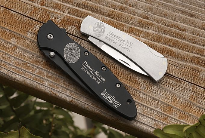 Two closed folding knives, one black and one silver, on a wooden surface