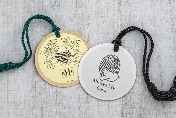 Two round engraved pendants with green and black cords on a light wood surface.
