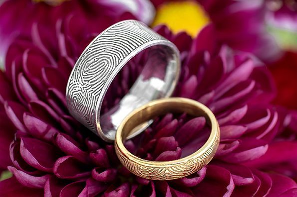 Two patterned rings, silver and gold, resting on a purple flower bloom