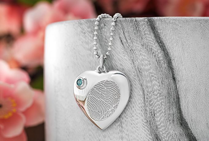 Heart-shaped silver pendant necklace with a fingerprint design and small gem on a marble background