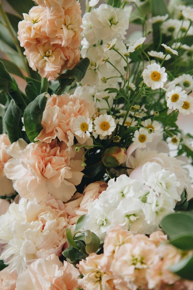 Peach, white, and cream flowers arranged with green foliage and small white daisies