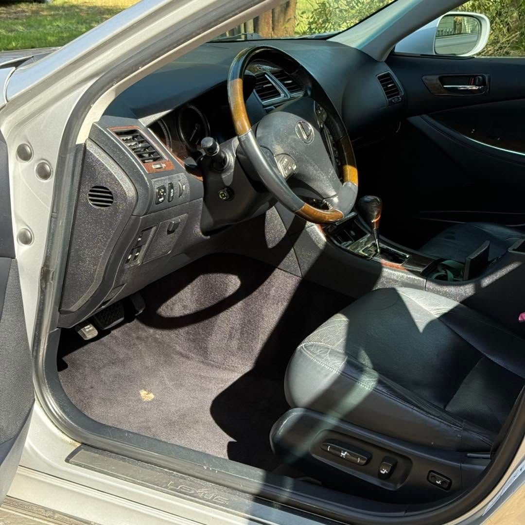 Car interior with driver’s door open, showing black leather seats, steering wheel, and dashboard in sunlight