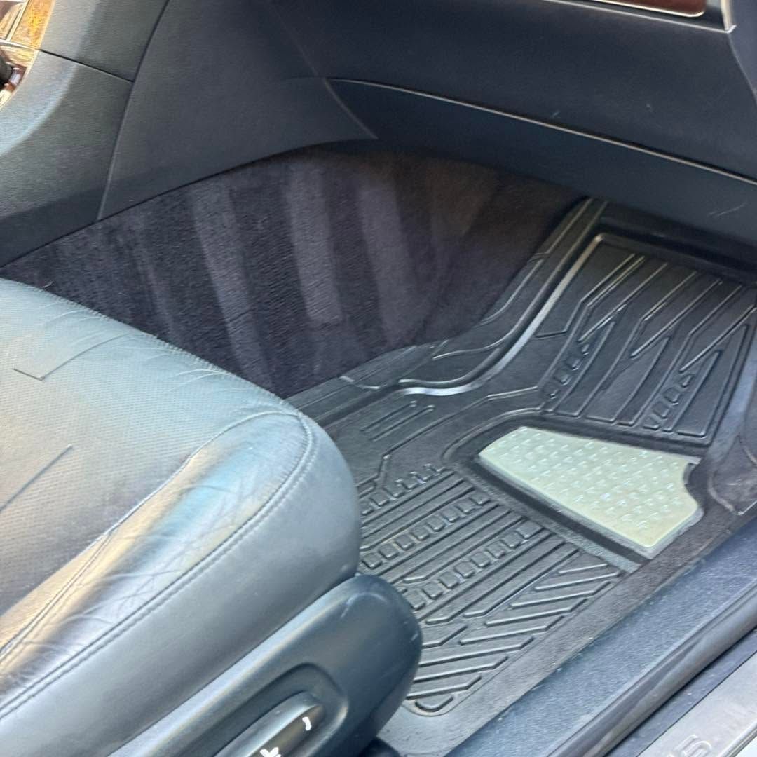Car interior footwell with black floor mat and light gray seat edge