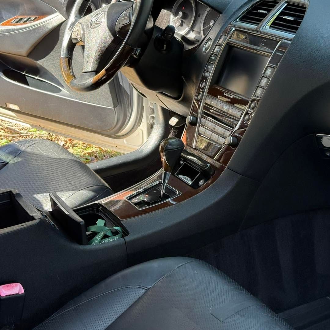 Luxury car interior with open driver door and exposed center console wiring, black seats, and wood trim