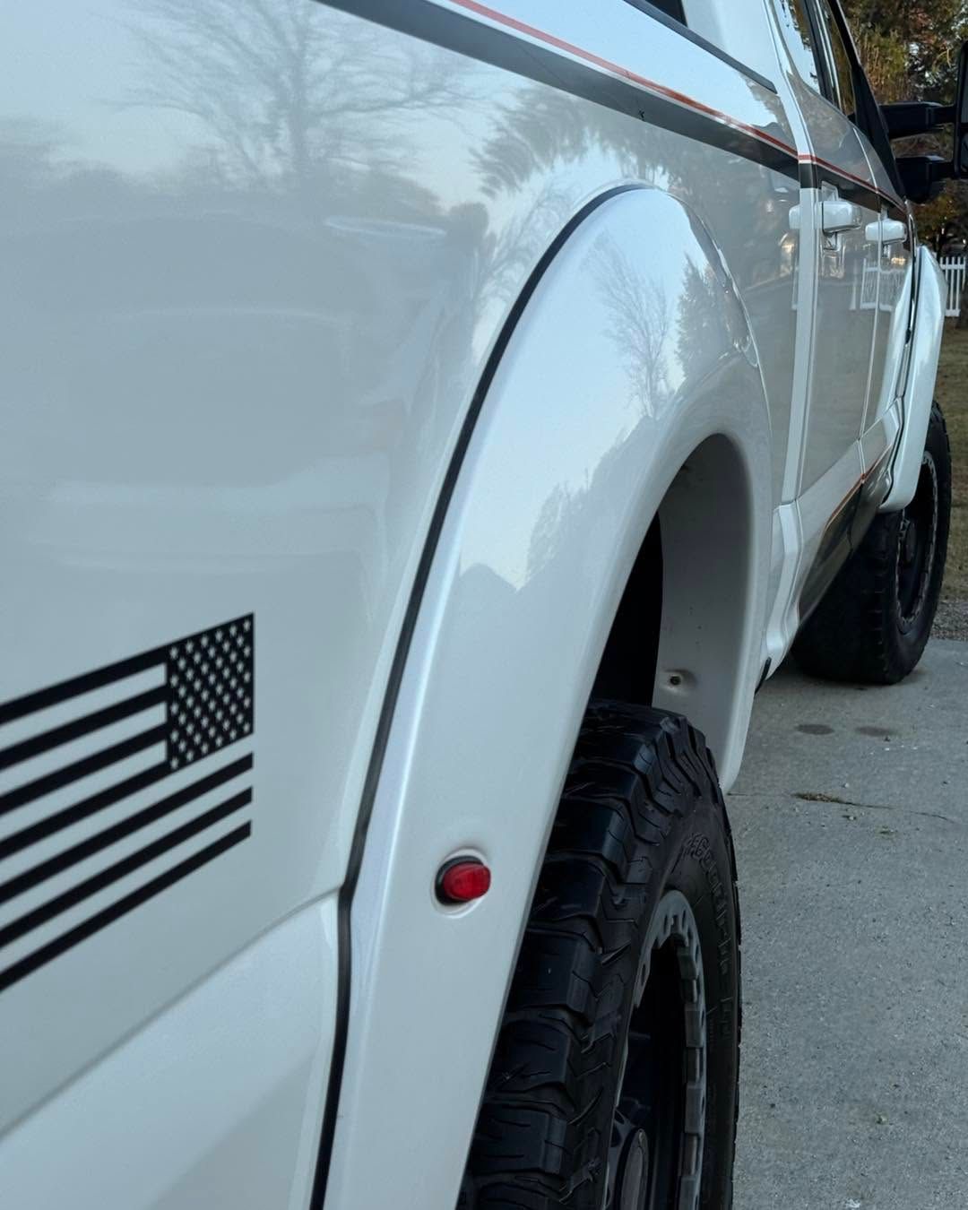 Close-up of a white off-road truck’s rear fender and tire with a black stripe decal on the side.