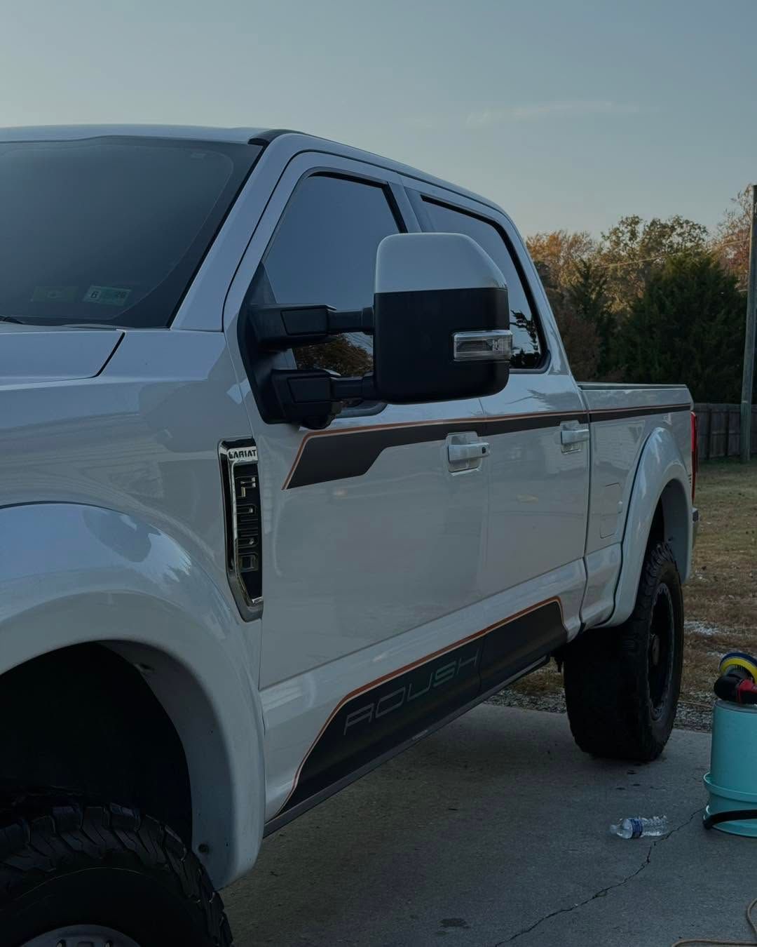 White pickup truck parked outdoors at dusk, side view with large black side mirror.