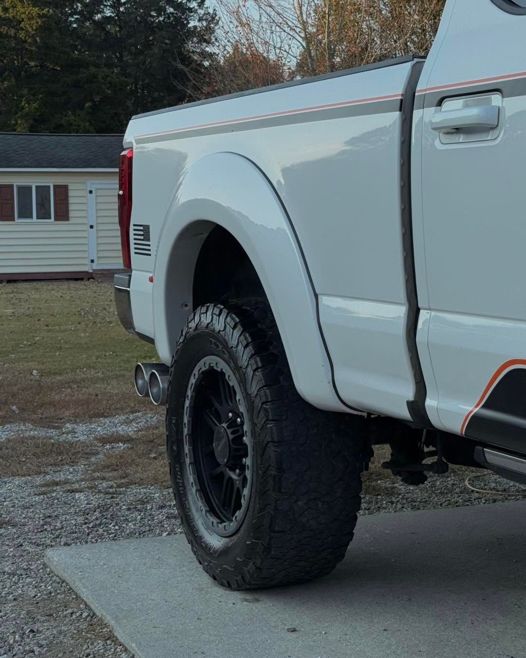 White pickup truck with off-road tires parked on a driveway near a house