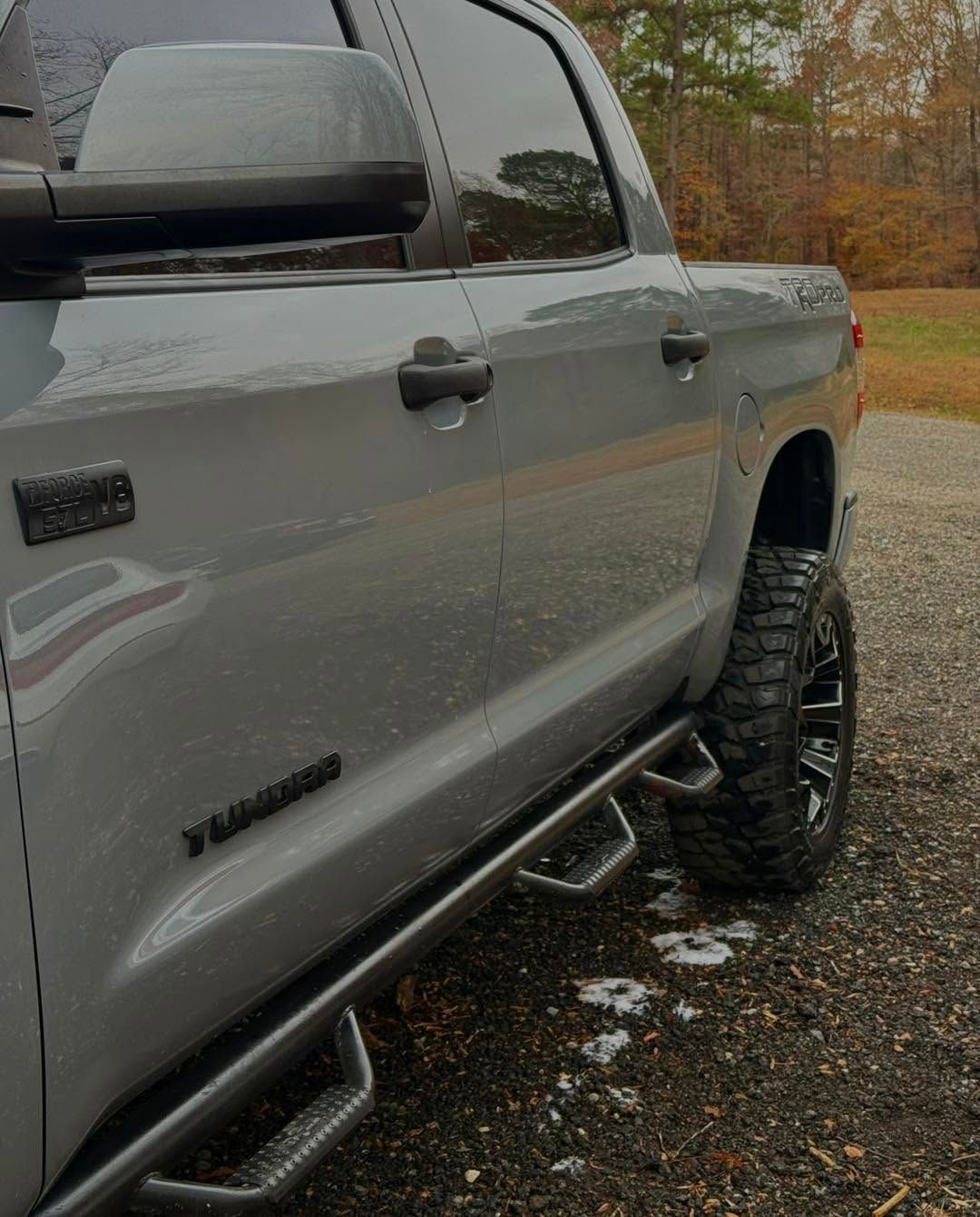 Gray pickup truck parked on wet gravel, shown from the side with black running boards and off-road tires