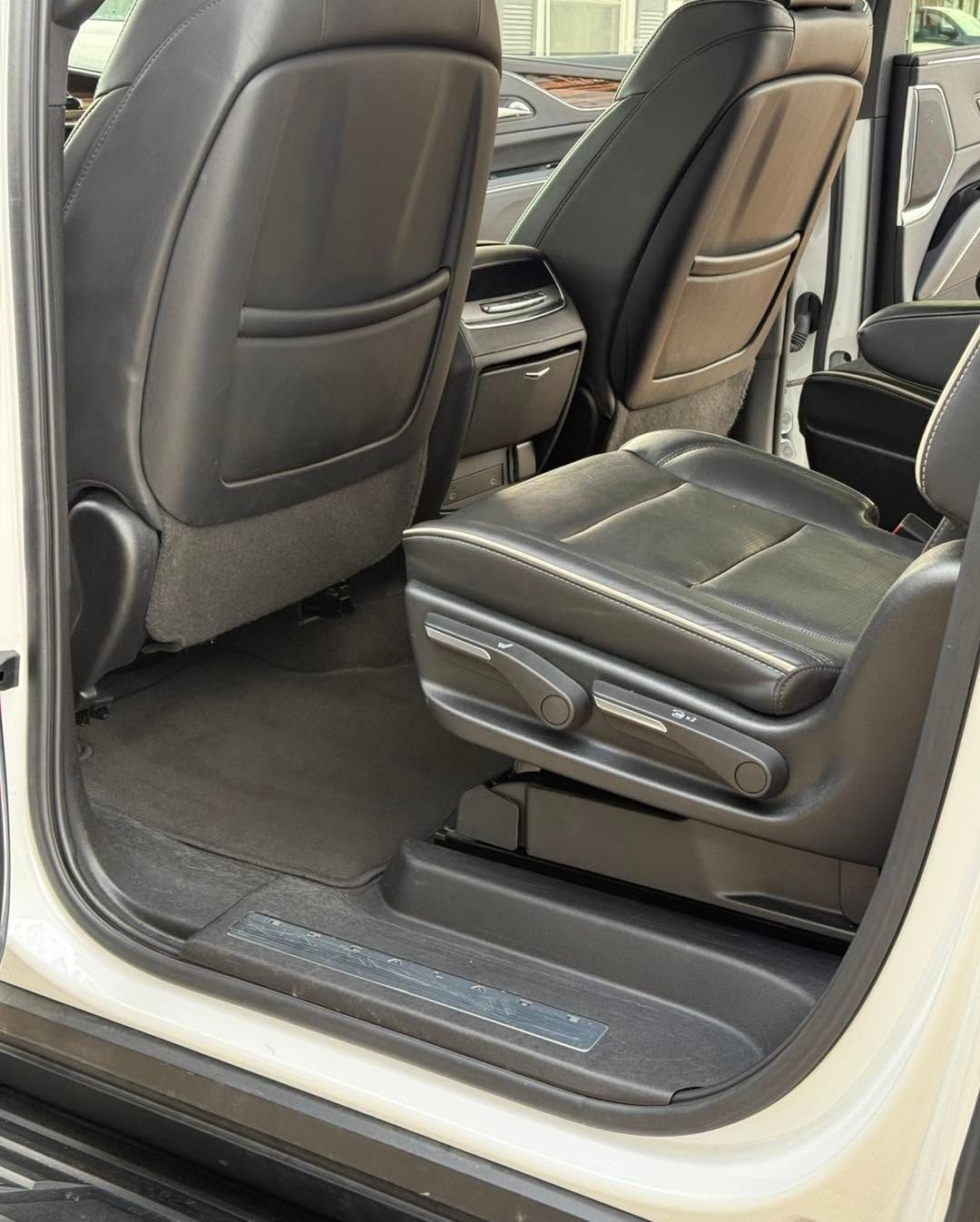 Second-row car seats with black leather upholstery and folding center armrest, viewed from an open door