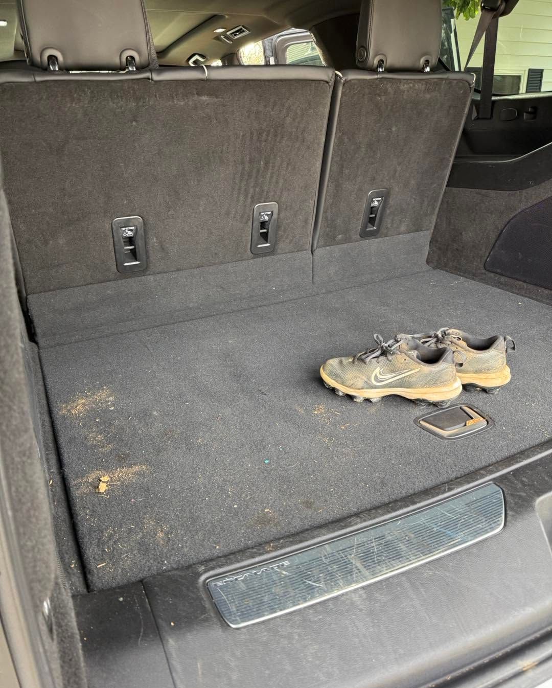 Car trunk cargo area with folded seats and a pair of shoes on the floor mat
