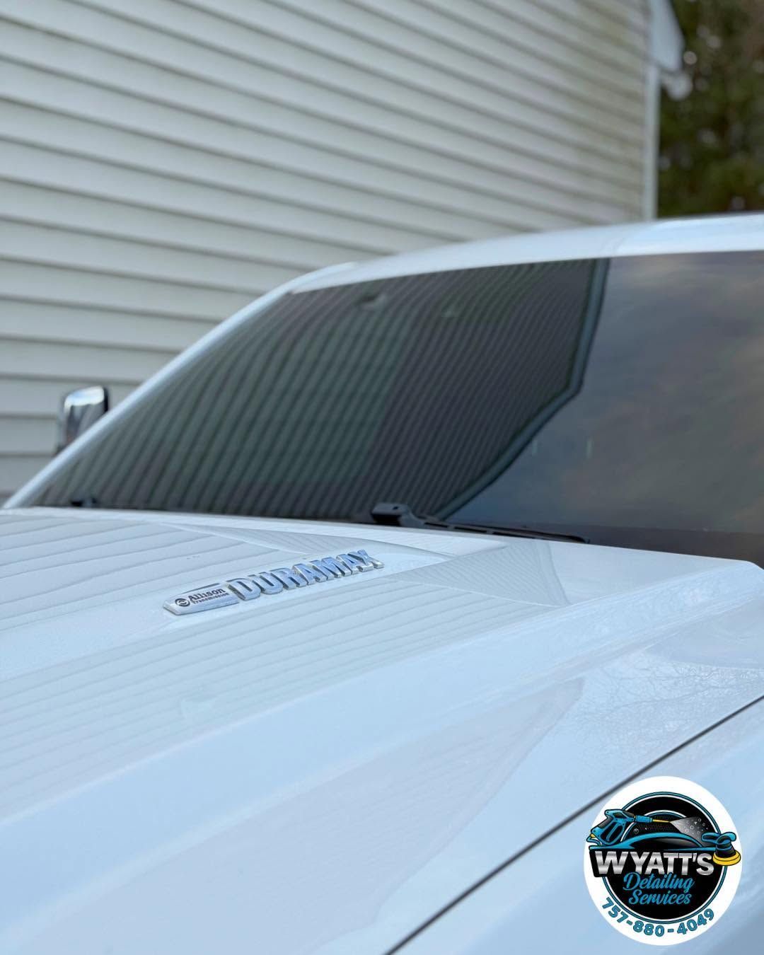 White car windshield and hood with tinted glass, parked beside a house with a WYATT badge on the lower right.