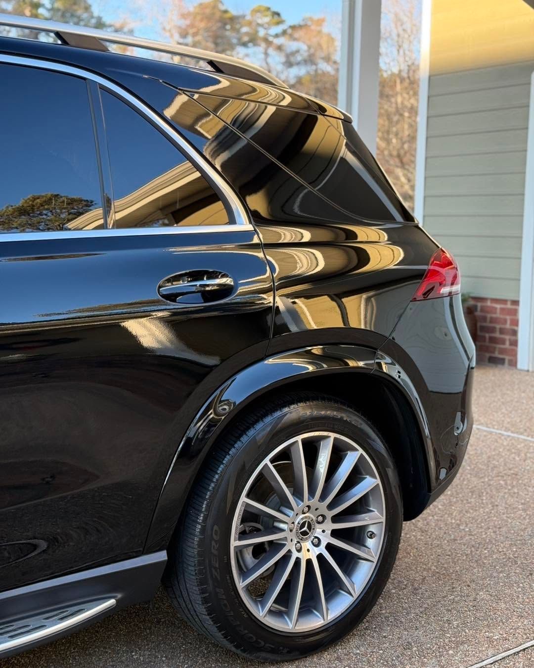 Black SUV parked on a driveway beside a house, rear side view with chrome wheels