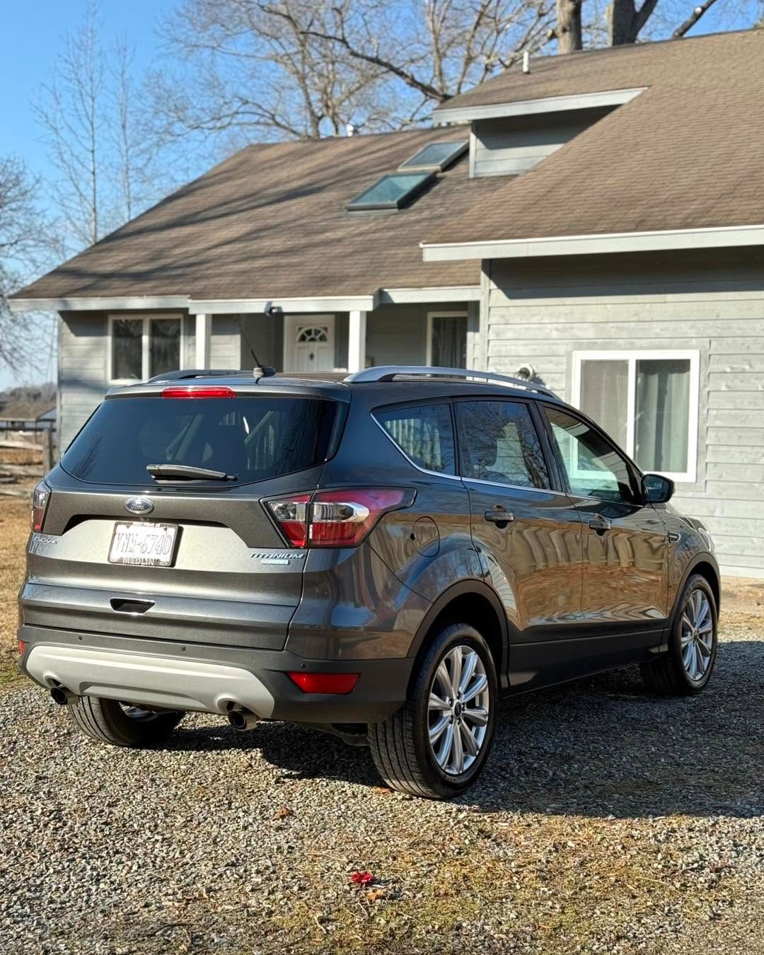 Brown SUV parked on a gravel driveway beside a light-colored house under a clear blue sky