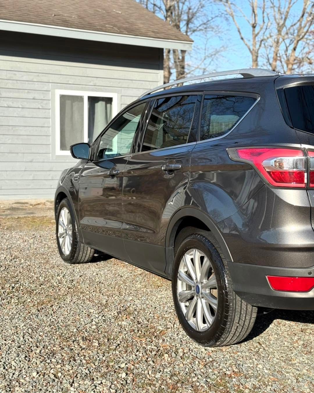 Dark gray SUV parked on a gravel driveway beside a house on a sunny day