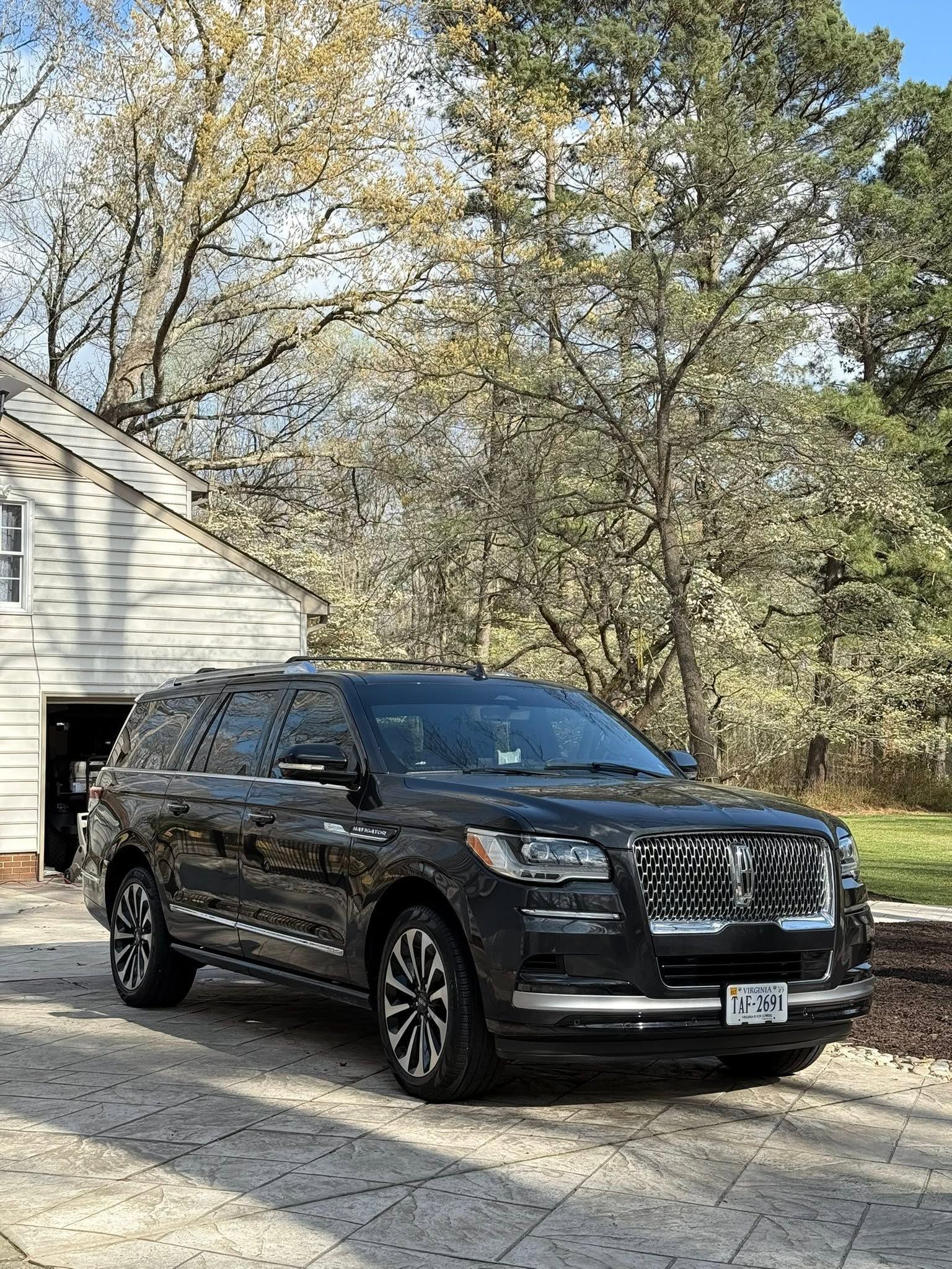 Black SUV parked on a driveway beside a house with trees in the background