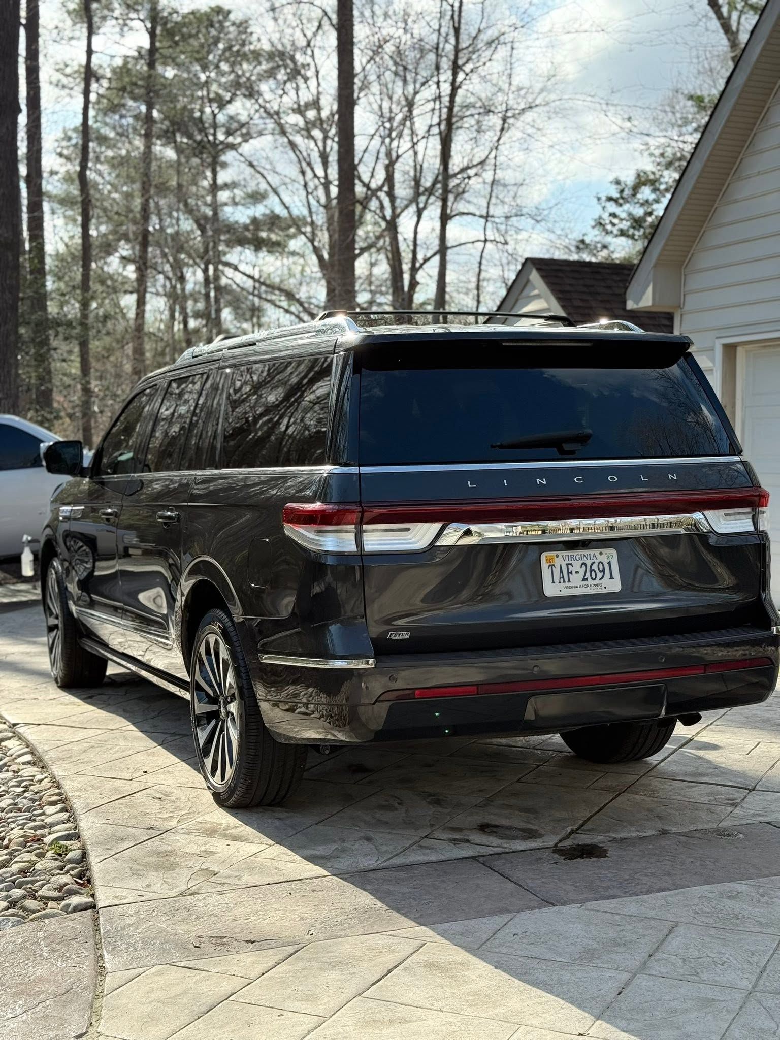 Black SUV parked in a driveway beside a house, with trees and a partly cloudy sky in the background.