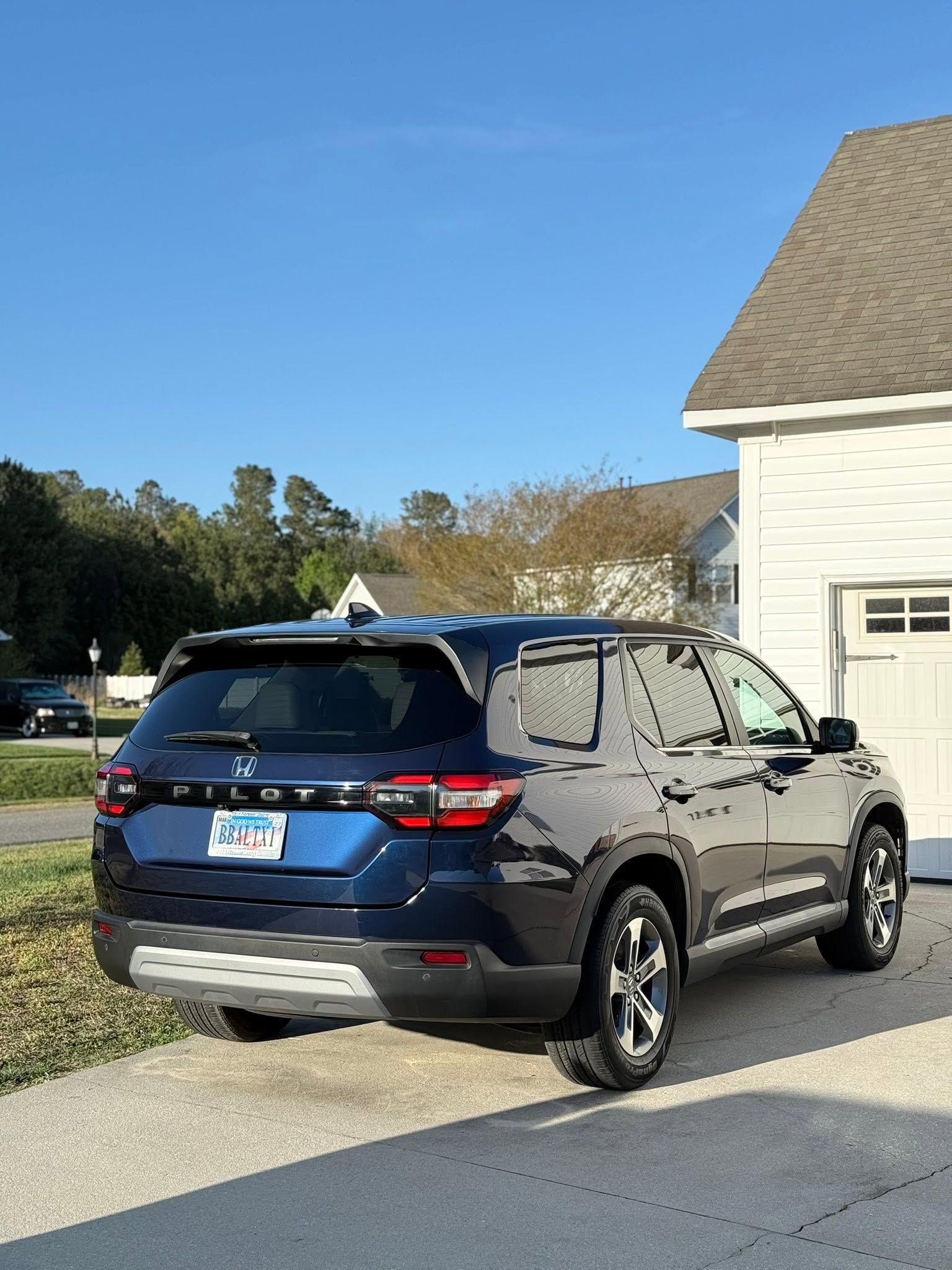 Blue SUV parked in a driveway beside a house on a sunny day