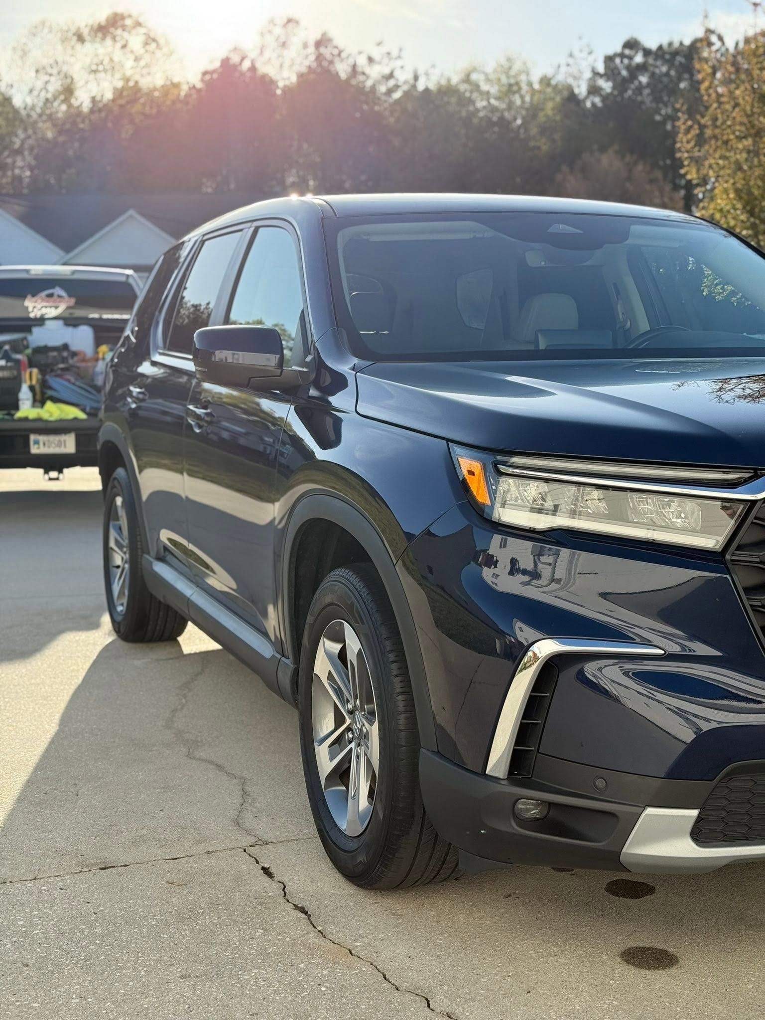 Dark blue SUV parked in a driveway at sunset, with a trailer and house in the background