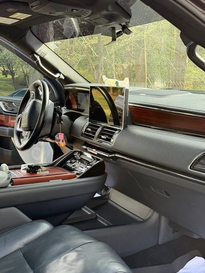 Luxury car interior with front passenger seat removed and dashboard folded open, showing electronics and wood trim.