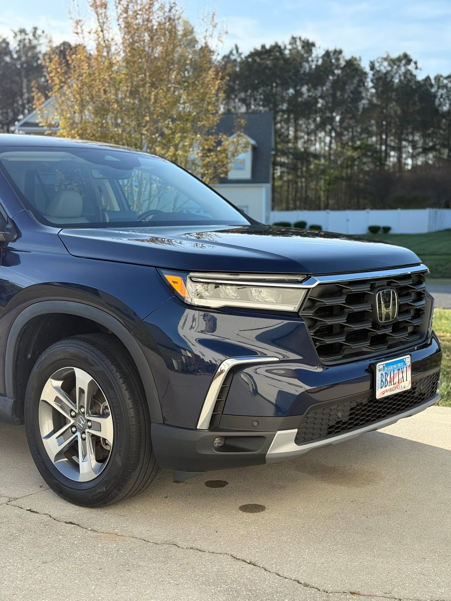 Blue SUV parked outdoors in front of trees and a house in daylight