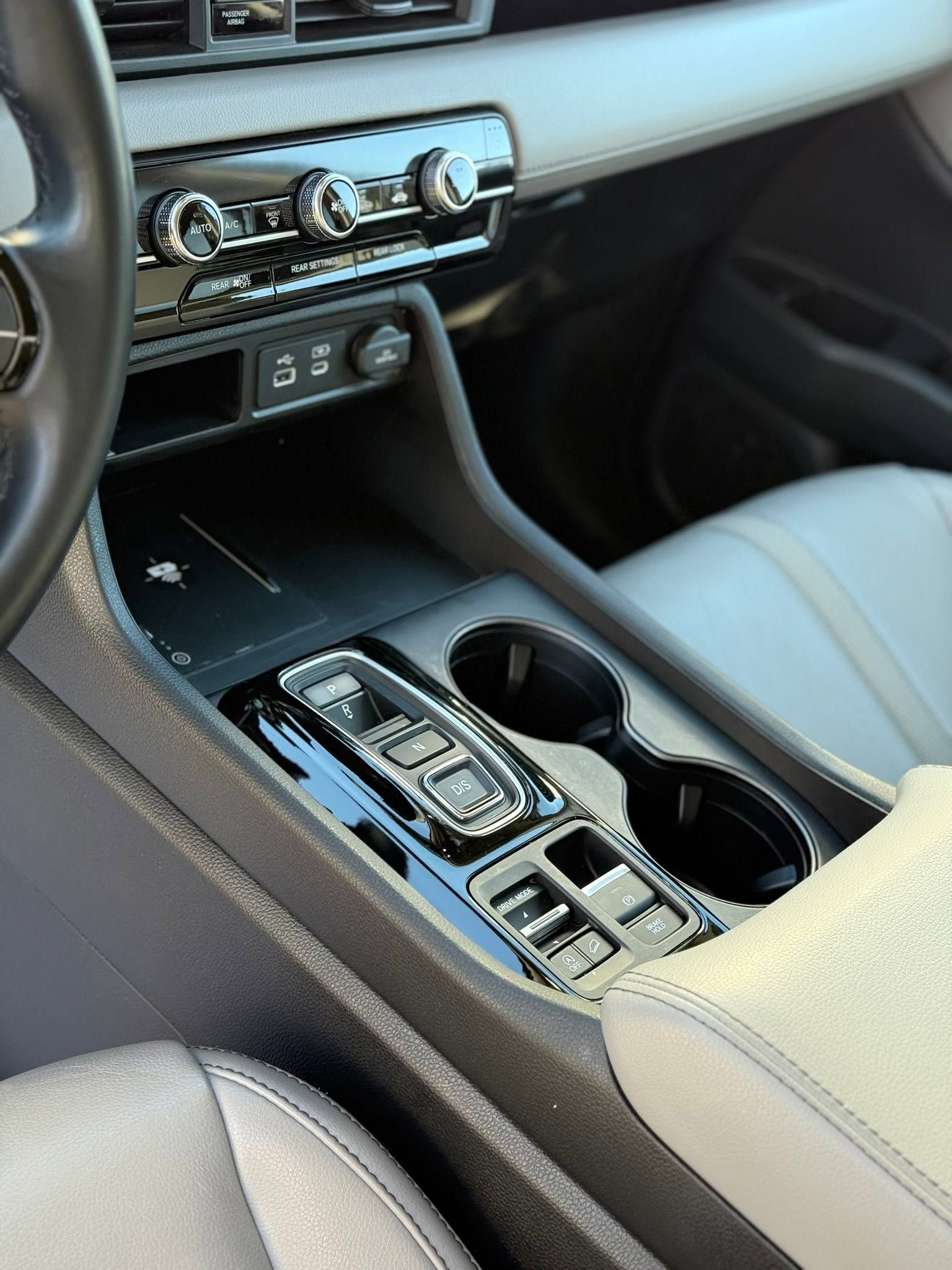 Car interior with center console, gear selector, cup holders, and climate controls in gray and black.