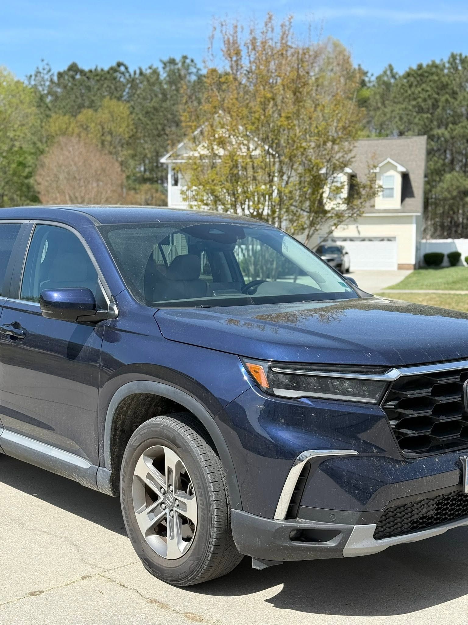 Blue SUV parked in a driveway in front of a suburban house and trees