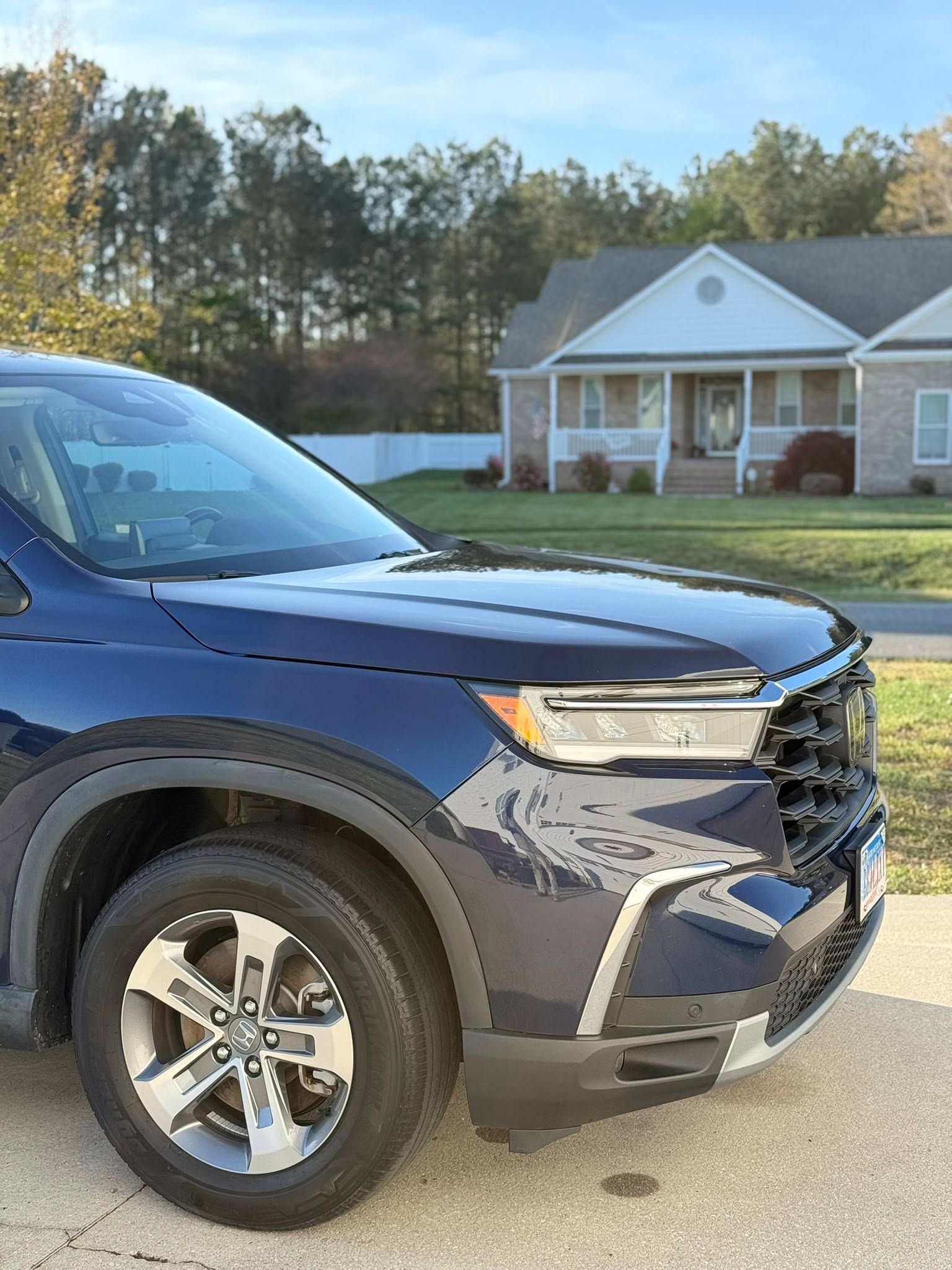 Blue SUV parked in front of a suburban house with a porch and trees in the background