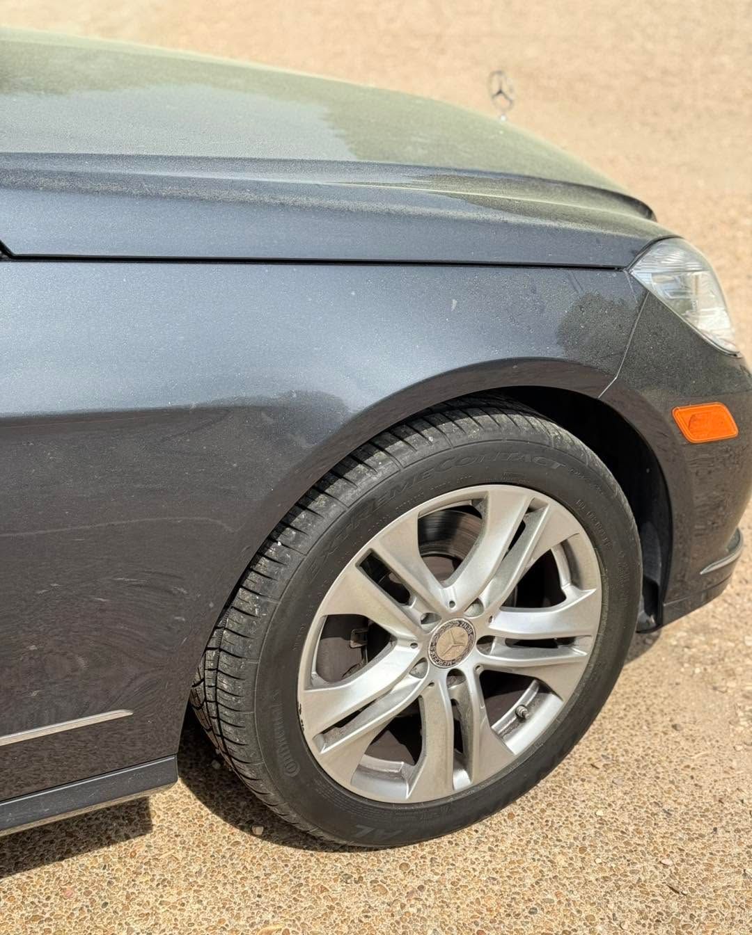 Close-up of a gray car’s front side and wheel parked on pavement