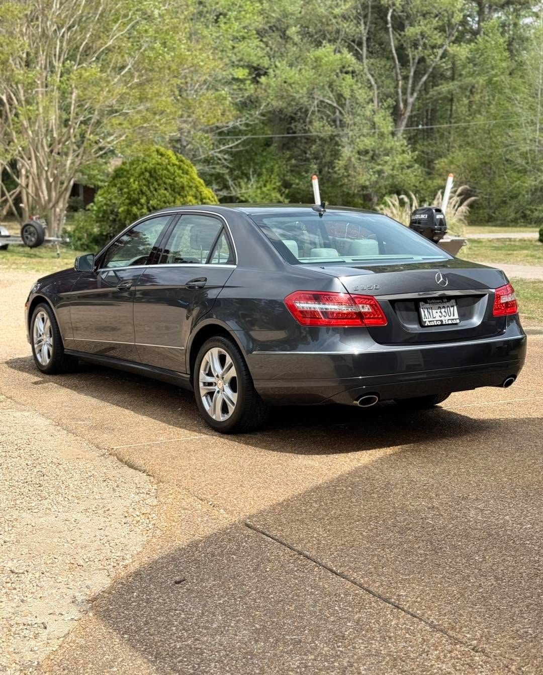 Dark gray sedan parked on a gravel driveway near a wooded area