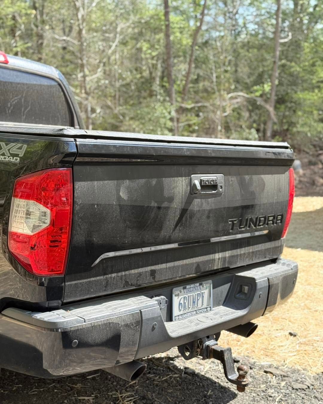 Black GMC pickup truck rear with tailgate, tow hitch, and a dirty bumper parked on a dirt road