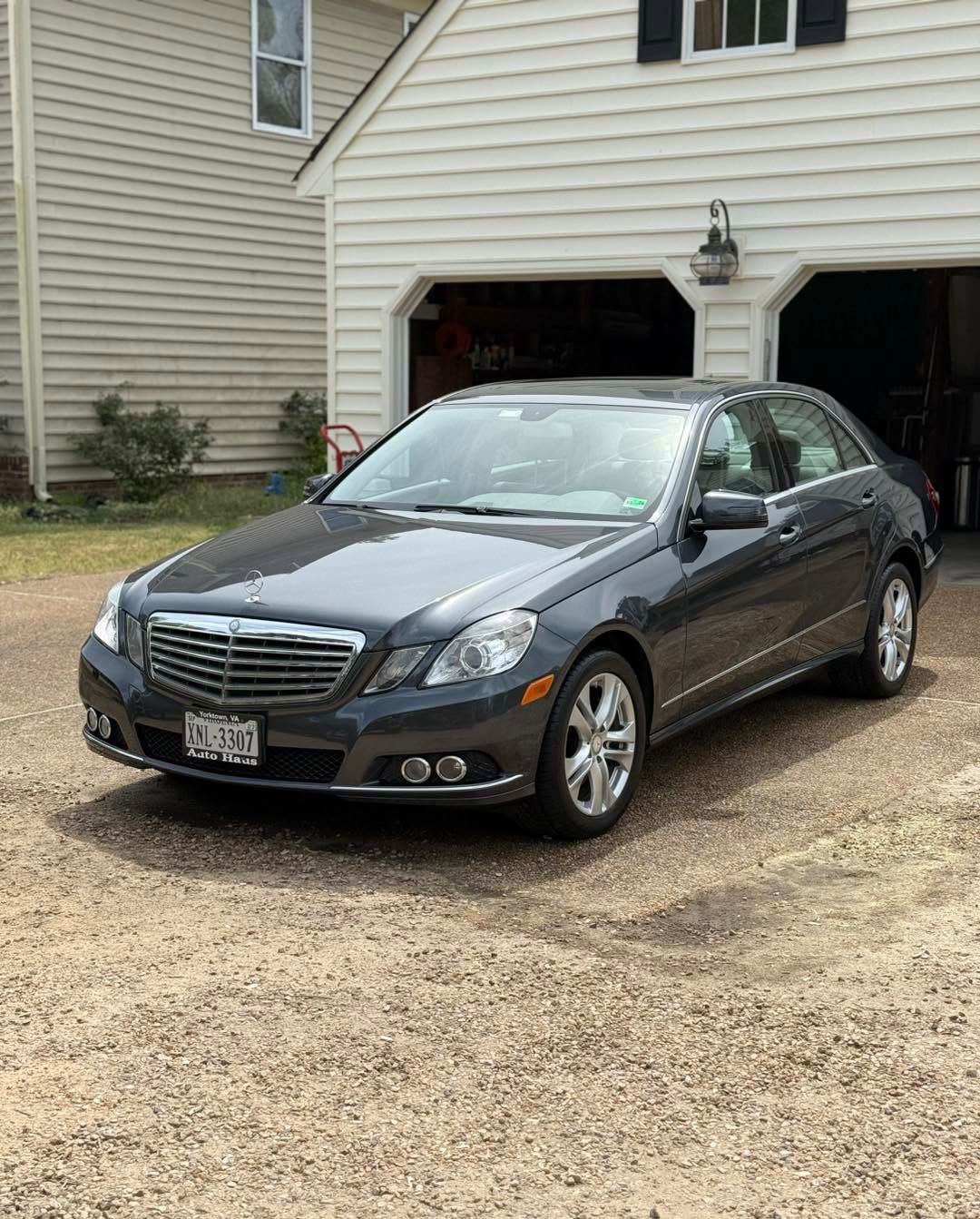 Dark gray sedan parked on a gravel driveway in front of a house garage