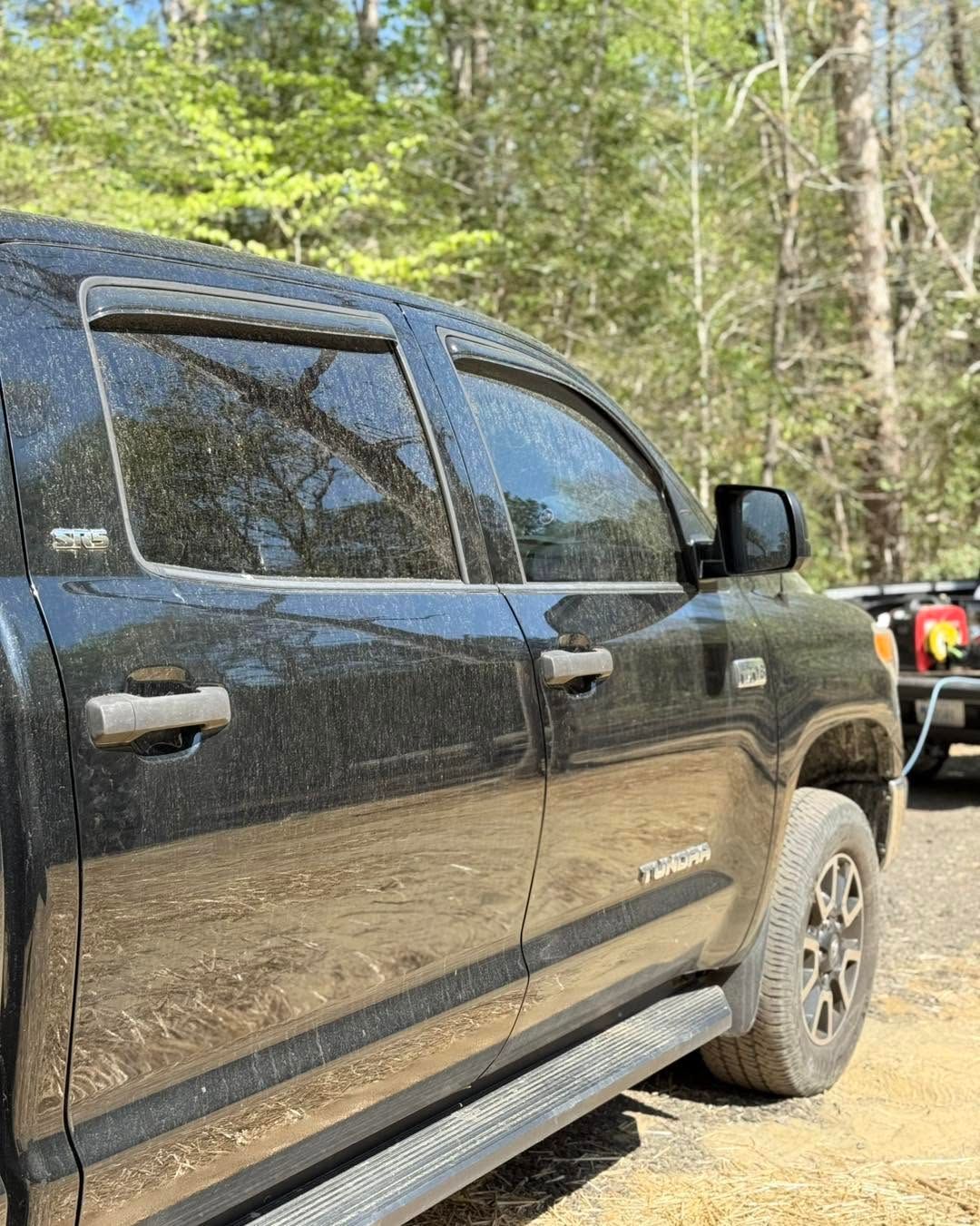 Black pickup truck parked on a dirt trail in a wooded area, side view.