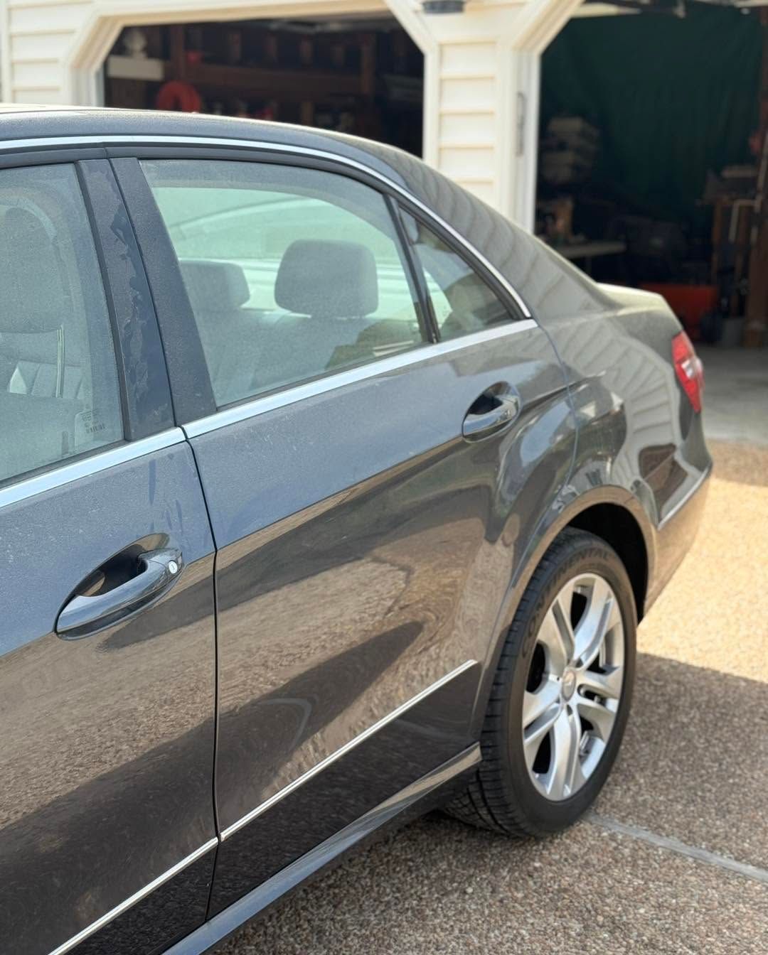 Gray sedan parked in a driveway outside a garage, rear side visible