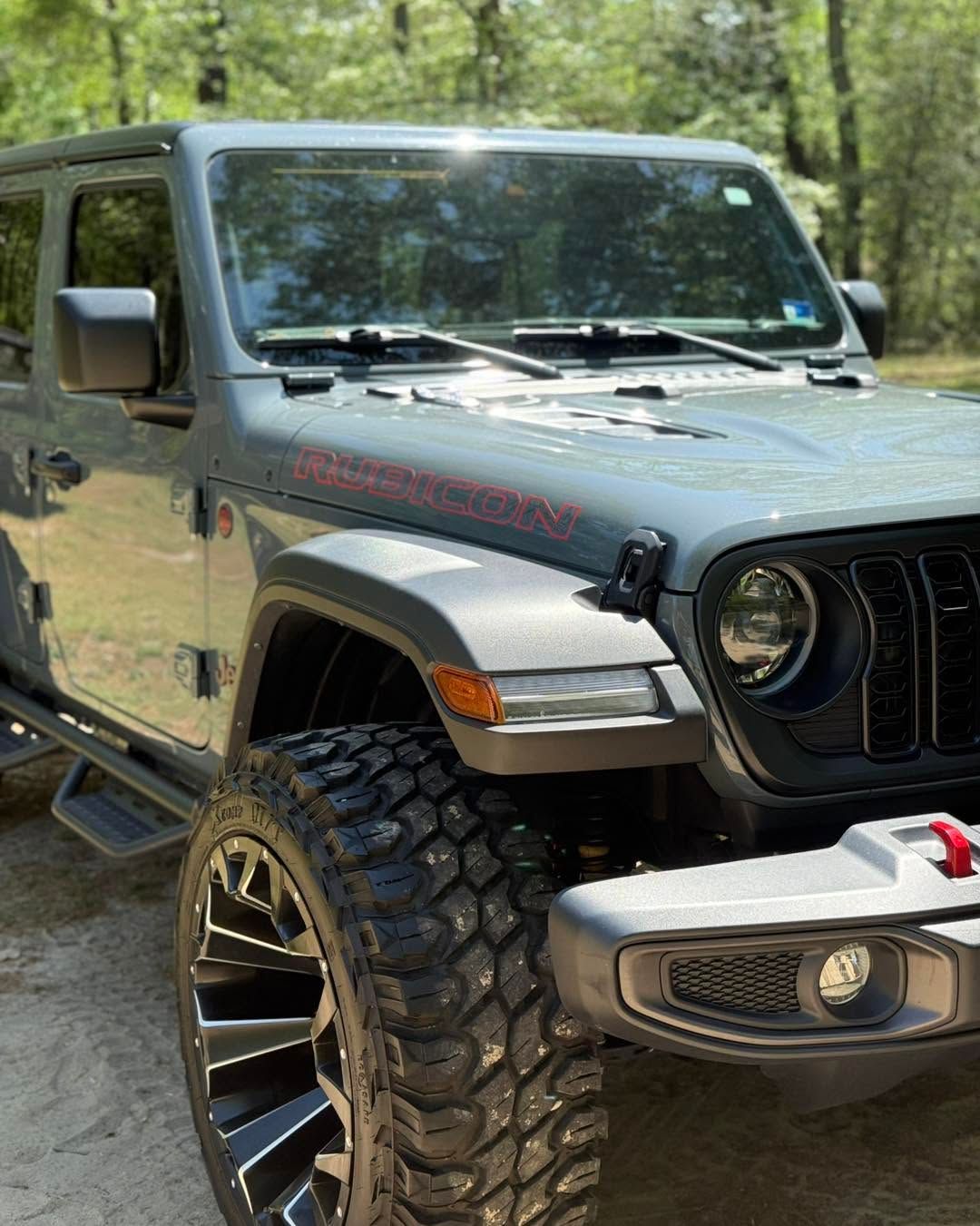 Gray Jeep Wrangler with large off-road tires parked on a wooded trail