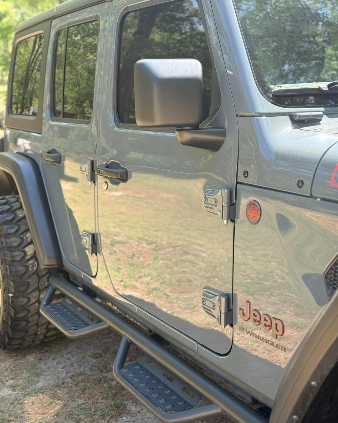 Gray Jeep Wrangler parked outdoors, showing side doors, black wheels, and running boards.