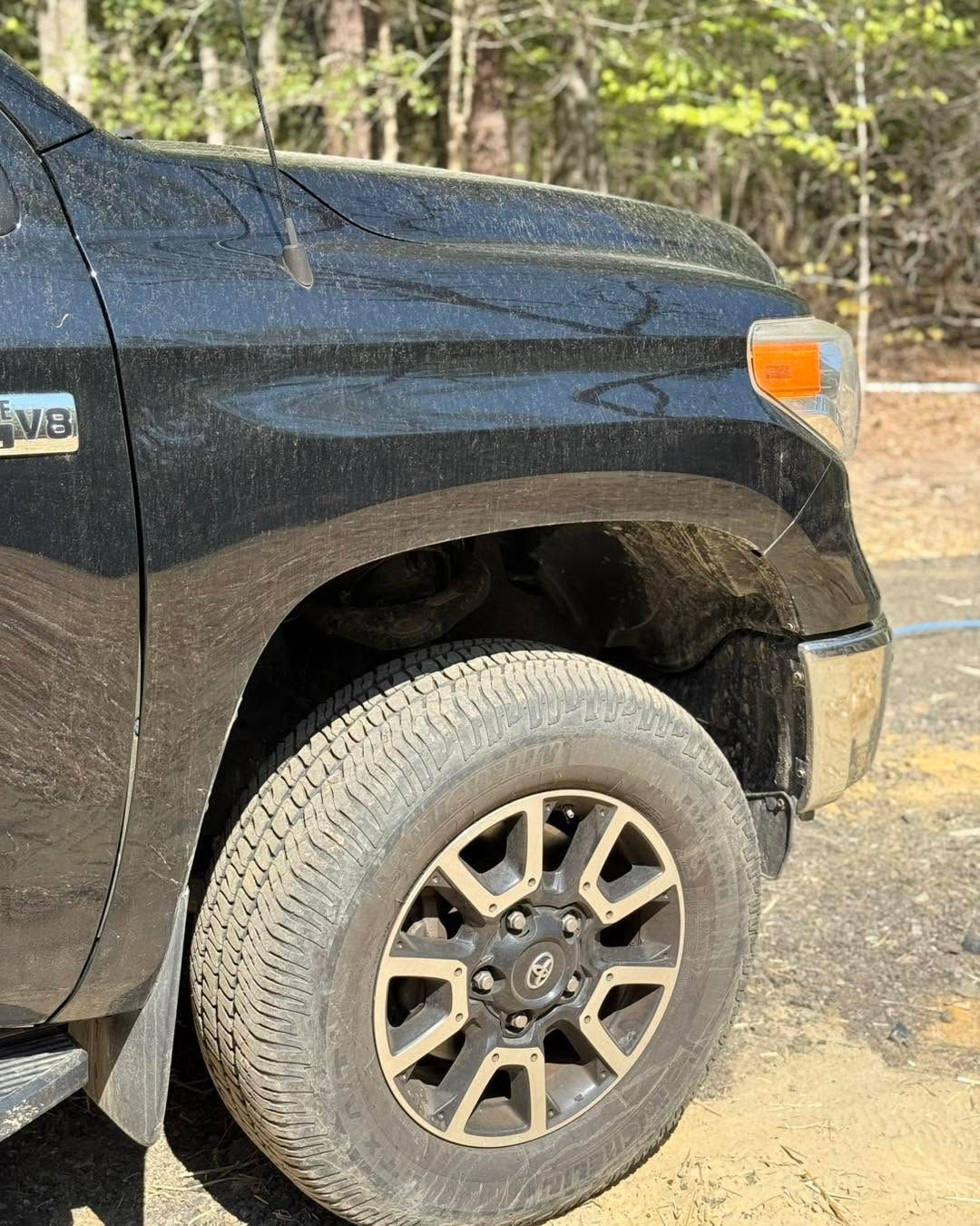 Close-up of a black pickup truck’s front wheel and fender on a dirt road.