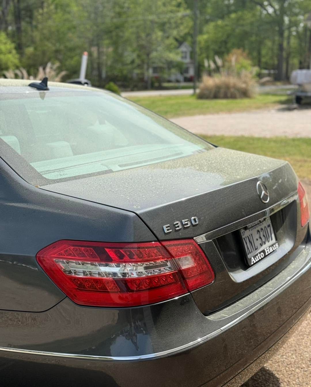 Rear view of a gray Mercedes E350 sedan parked outdoors in a leafy area