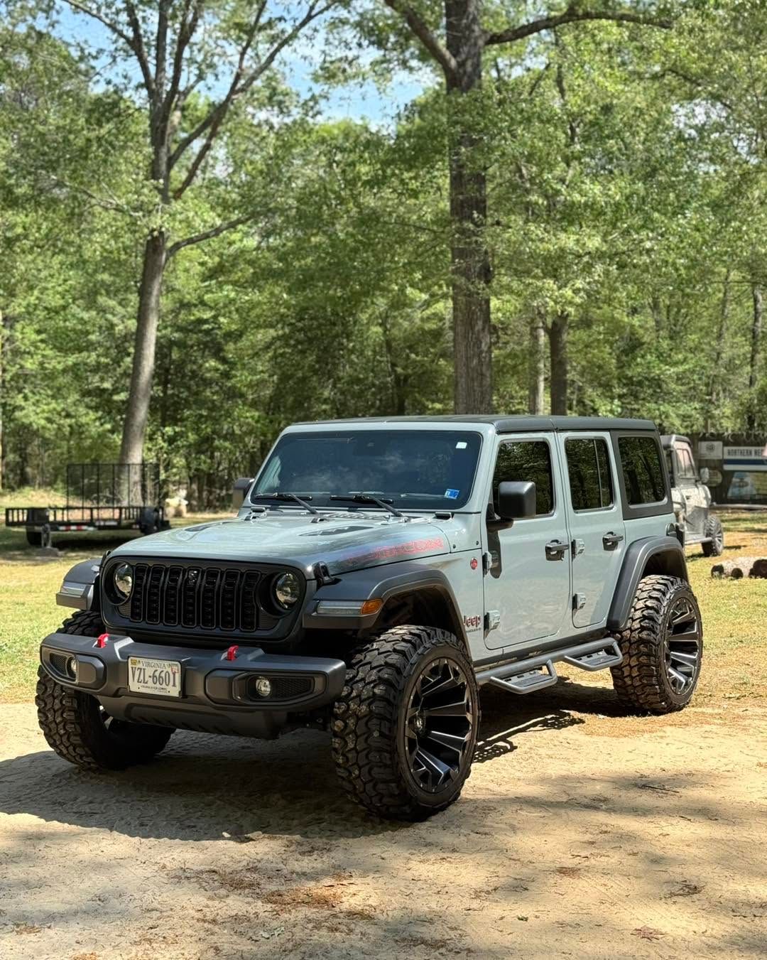 Gray lifted Jeep Wrangler parked on a dirt path in a wooded area