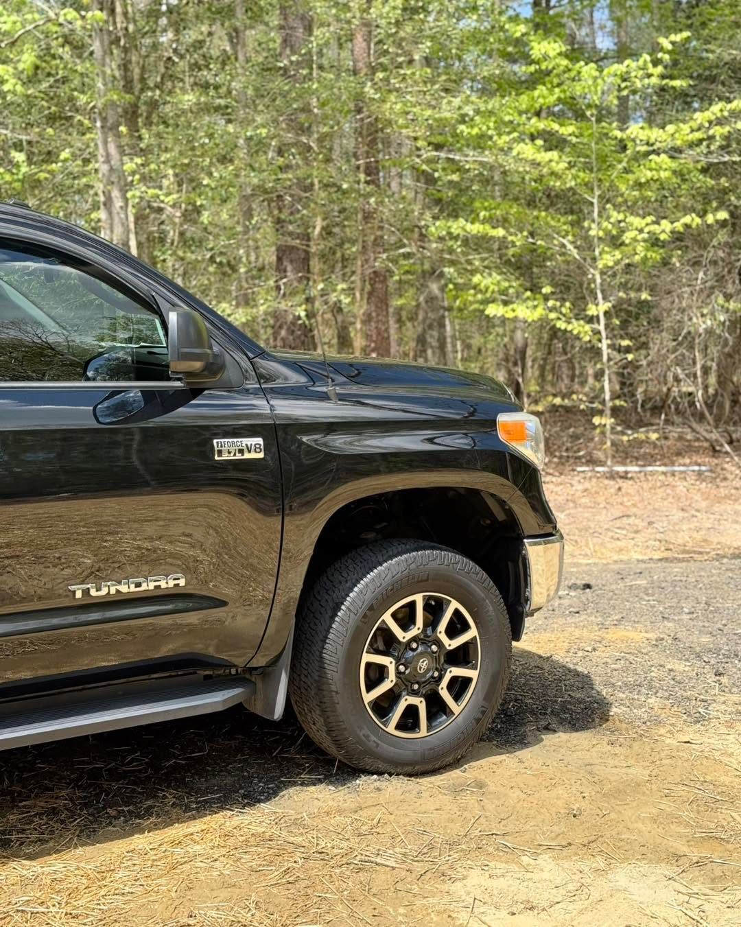 Black Toyota Tundra parked on a gravel road beside a wooded area.