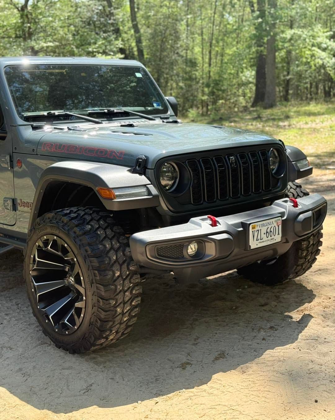 Black Jeep Wrangler on a dirt trail in a wooded area, front view with large off-road tires and bumper
