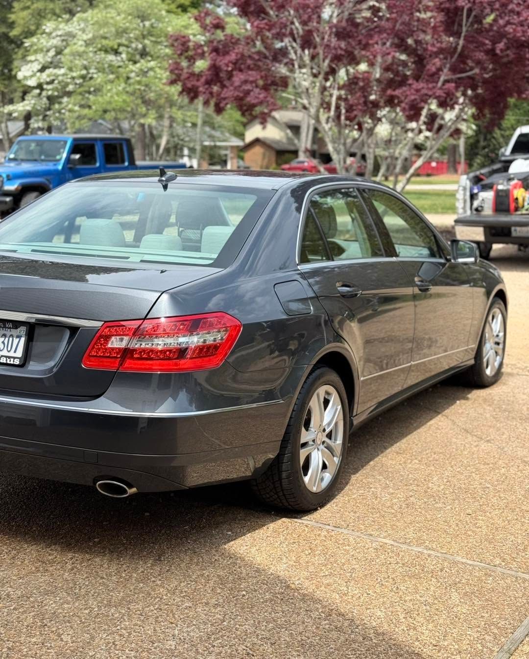 Black sedan parked on a driveway with trees and other cars in the background.