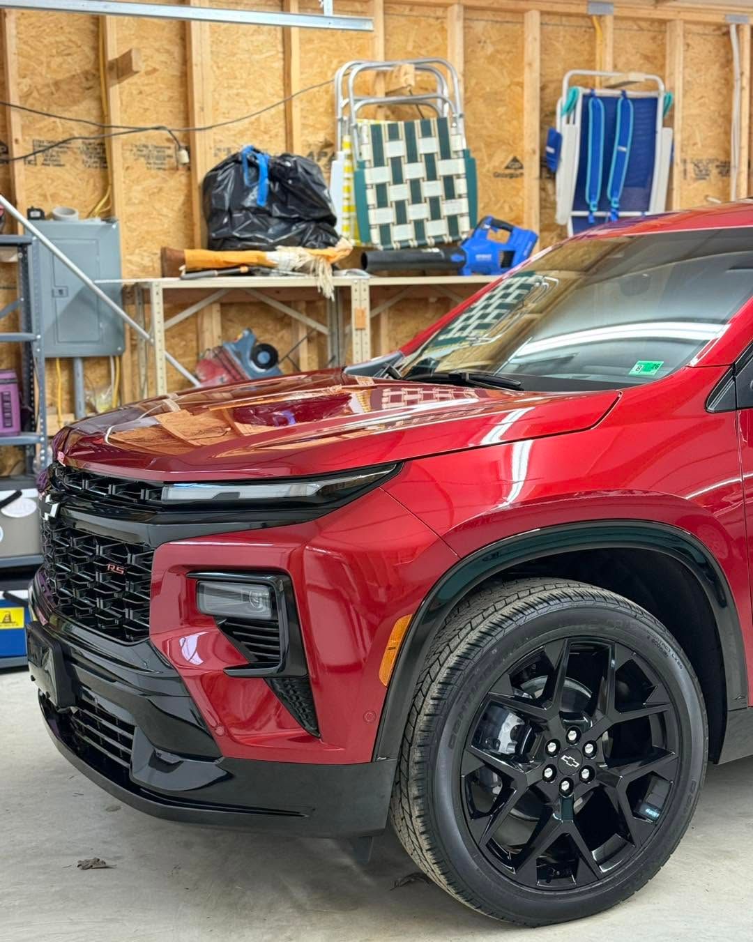 Red SUV parked in a garage with black wheels and a wooden wall behind it