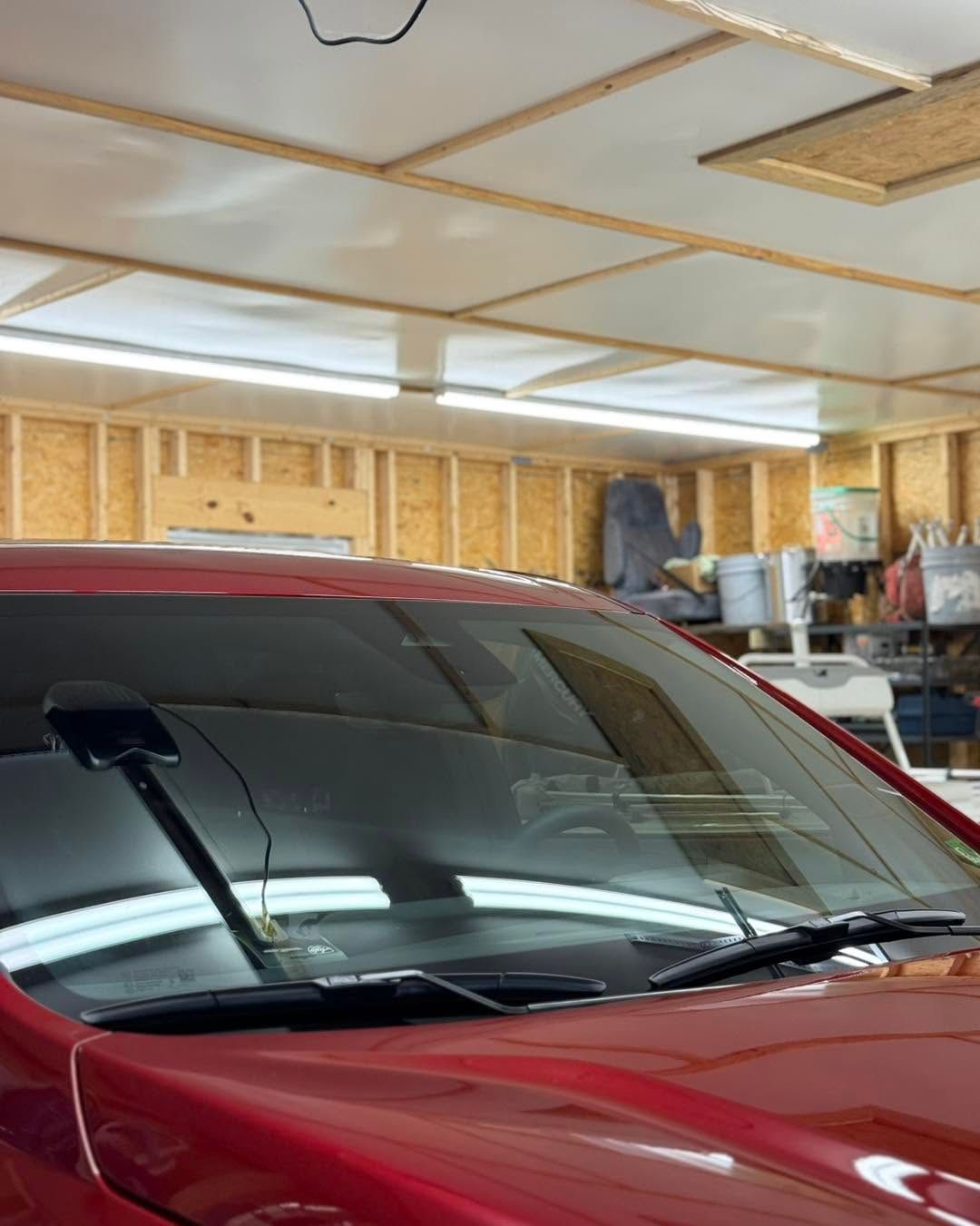 Red SUV parked in a garage with unfinished walls and ceiling panels above.