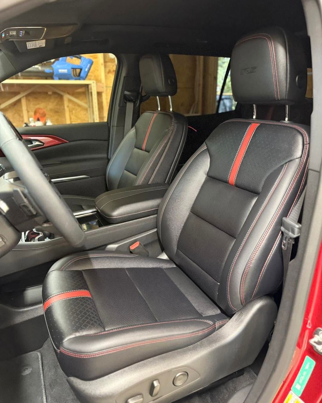 Black leather car seats with red accents inside a red vehicle, shown from the front passenger side