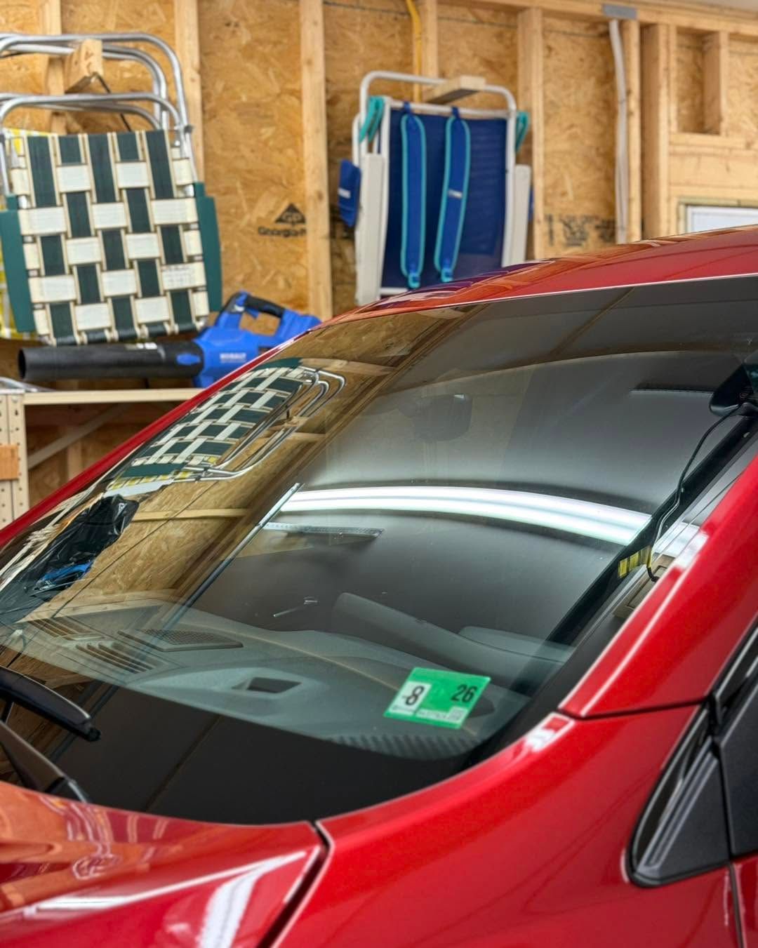 Red car parked in a garage beside folded chairs and a checkered bag
