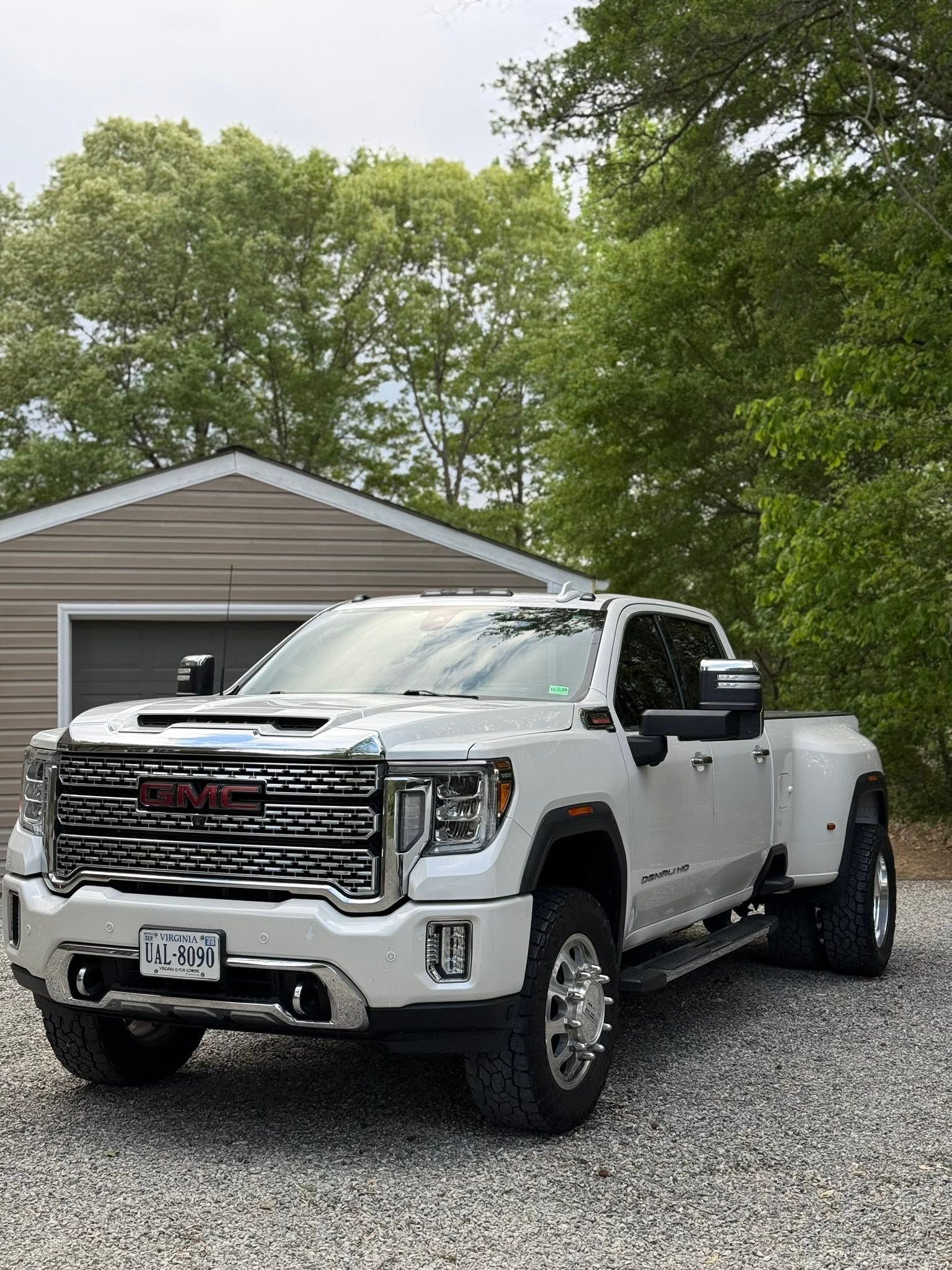 White GMC pickup truck parked on gravel in front of a gray garage with trees overhead